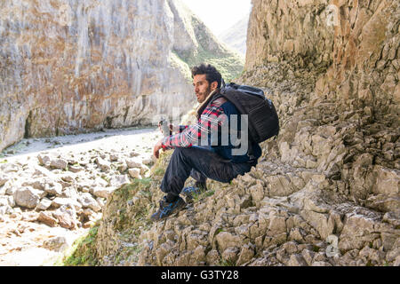 Un alpinista seduto con una bottiglia di acqua in un terreno accidentato. Foto Stock