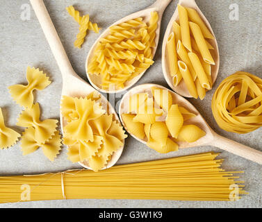 Vari tipi di pasta in cucchiai di legno sul tavolo di pietra, vista dall'alto Foto Stock