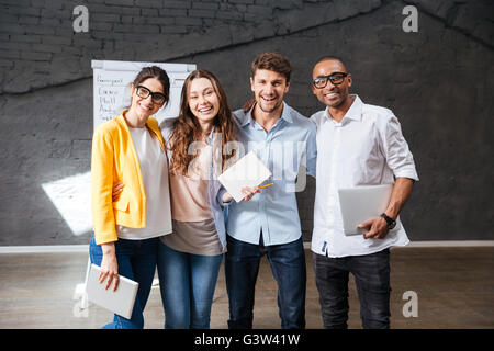 Gruppo multietnico di felice young business persone azienda tablet e laptop in piedi in ufficio Foto Stock