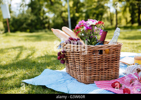 Vista dettagliata del cesto per pic-nic con bevande, cibo e fiori sull'erba Foto Stock