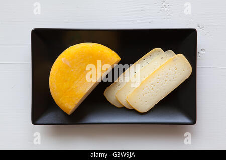 Ceramica Nera piatti rettangolo con blocco di gustoso formaggio isolato su bianco scrivania in legno Foto Stock