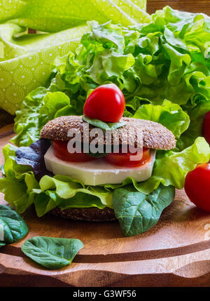 Burger: vegan burger con lattuga, freschi pomodori ciliegia e formaggio feta su sfondo di legno. Foto Stock