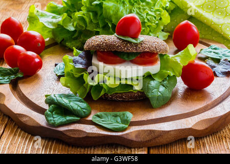 Burger: vegan burger con lattuga, freschi pomodori ciliegia e formaggio feta su sfondo di legno. Foto Stock
