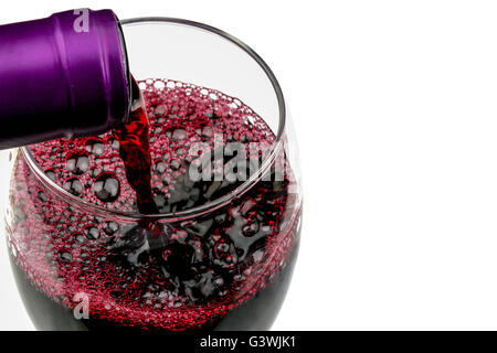 Immagine creativa di versare il vino rosso da una bottiglia di un vetro isolato contro uno sfondo bianco con spazio di copia Foto Stock