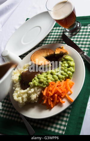 Un classico inglese tradizionale piatto di bistecche, torta di purè di patate, fiacco piselli e carote. Serviti con sugo di carne e un bicchiere di birra. Foto Stock