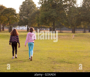 Rubrica Home. Due giovani sorelle camminare insieme verso l'uscita del parco. Il sole tramonta e la sera è il disegno a. Foto Stock