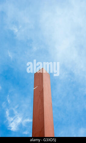 Singola piazza marrone pole di raggiungere in poco nuvoloso cielo blu in prospettiva. Foto Stock