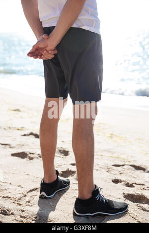 Primo piano delle gambe del giovane uomo in pantaloncini corti e scarpe da ginnastica permanente sulla spiaggia Foto Stock