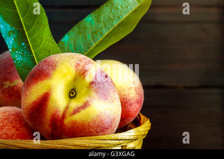 Le pesche in intessute cesto su legno scuro dello sfondo. Spazio di copia Foto Stock