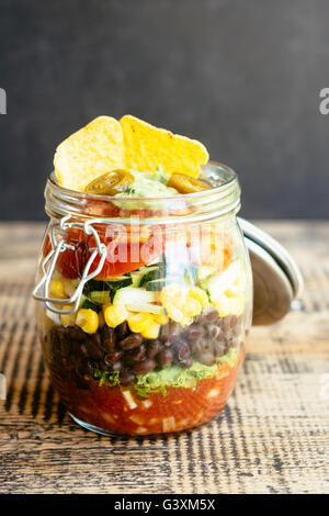 Insalata messicana in un vasetto con salsa, lattuga, fagioli neri, mais, zucchine, pomodori, guacamole, taco trucioli e jalapeno Foto Stock