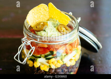 Insalata messicana in un vasetto con salsa, lattuga, fagioli neri, mais, zucchine, pomodori, guacamole, taco trucioli e jalapeno Foto Stock