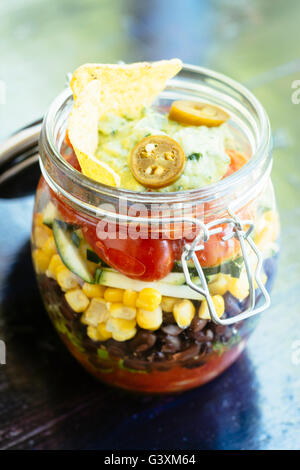 Insalata messicana in un vasetto con salsa, lattuga, fagioli neri, mais, zucchine, pomodori, guacamole, taco trucioli e jalapeno Foto Stock