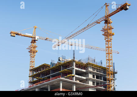 Alto edificio sito in costruzione di gru contro il cielo blu sullo sfondo Foto Stock