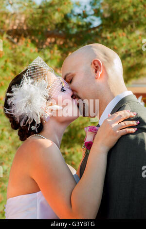 La sposa e lo sposo durante il loro primo bacio come una coppia sposata. La sposa indossa una birdcage Veil. Foto Stock