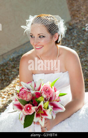 Un Recentemente sposato sposa squat verso il basso per fare una breve pausa da dolorose scarpe. Lei ha un sorriso sul suo viso e un bel bouquet Foto Stock