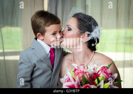 Una giovane sposa bacia il figlio il giorno del matrimonio nella sua pre-ritratto di nozze. Ha conseguito il suo bouquet e si appoggia in per un bacio. Foto Stock