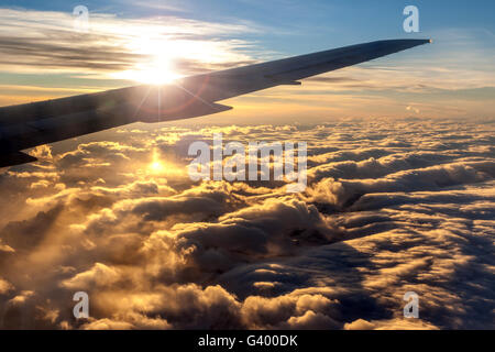 Vista di golden sunrise al di fuori della finestra di aereo con la deliberata lens flare su piano silhouette di parafango per effetto. Un mare di nubi Foto Stock