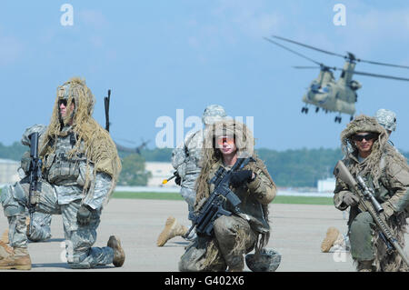 I soldati indossano tute ghillie prendere un ginocchio come un CH-47 Chinook vola tettuccio Foto Stock