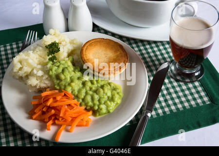 Un classico inglese tradizionale piatto di bistecche, torta di purè di patate, fiacco piselli e carote. Serviti con sugo di carne e un bicchiere di birra. Foto Stock