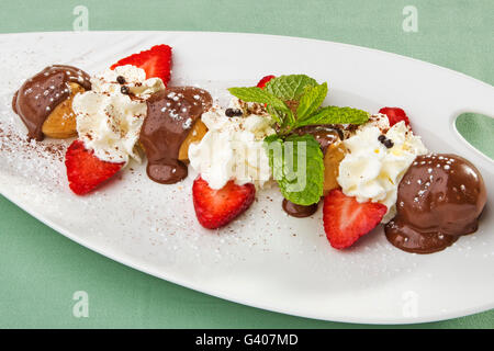 Il dessert. Profiteroles al cioccolato con salsa di panna e fragole fresche Foto Stock