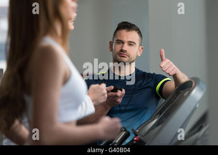 Personal Trainer che mostra Ok firmare al cliente - gruppo di persone che esercitano sul tapis roulant in palestra o Fitness Club Foto Stock