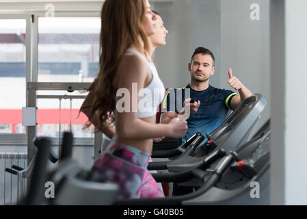 Personal Trainer che mostra Ok firmare al cliente - gruppo di persone che esercitano sul tapis roulant in palestra o Fitness Club Foto Stock