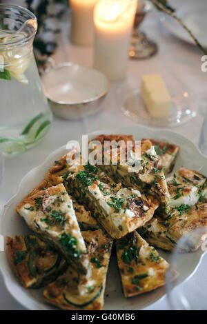 Frittata con verdure e formaggio di capra e un vaso di vetro di limone e lime infuso di acqua su un set up table per luce estate pranzo Foto Stock