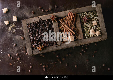 Verde e marrone e non torrefatto Caffè decaffeinato e nero caffè torrefatto in grani con spezie e cubetti di zucchero nella vecchia scatola di legno sopra il marrone scuro tex Foto Stock