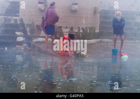 Unidentified donna indiana tenendo bagno rituale nel fiume Gange a nebbia fredda mattinata d'inverno. Foto Stock