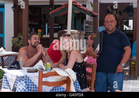 Coppia sorridente e cameriere al fiume vecchio taverna, la città di Kos, Kos (Cos), del Dodecaneso, Egeo Meridionale Regione, Grecia Foto Stock