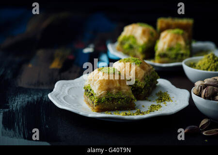 Il pistacchio baklava fettine su due piastre lungo con una ciotola di tutto il pistacchio e una ciotola di terra al pistacchio. Foto Stock