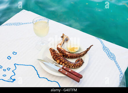 Polpo alla brace e vino bianco vetro su di un tavolo presso la costa del mare in un ristorante di piccole dimensioni su un isola greca di Kastellorizo Foto Stock
