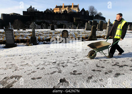 Un'operaia del consiglio lavora nel cimitero di Ballengeich con il castello di Stirling sullo sfondo a Stirling dopo la caduta della neve leggera nella zona. Foto Stock