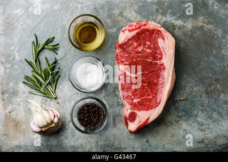 Materie carni fresche bistecca di controfiletto al rosmarino, olio, sale e pepe in pietra sullo sfondo di ardesia Foto Stock