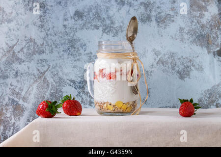 Sana colazione muesli, fragole e yogurt in vetro mason jar con cucchiaio. Yogurt servita su bianco tovaglia tessile con Foto Stock