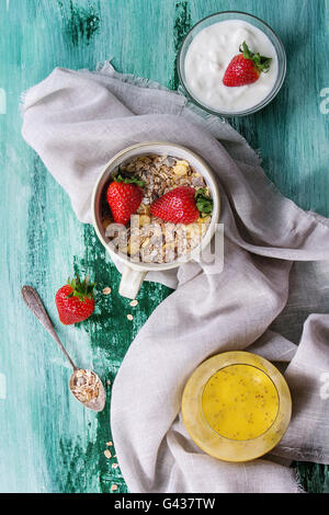 Ingredienti per una sana prima colazione. Yogurt, ciotola di muesli con fragole e bicchiere di mango smoothie con semi di chia su bianco Foto Stock