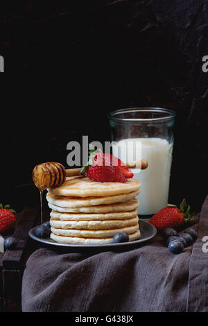 Pancake con fragole fresche e mirtilli in blu piastra in ceramica, e fluente dal miele Il miele in legno bilanciere, servita con Foto Stock