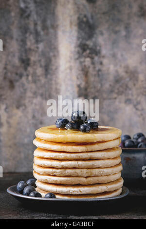 Pancake con mirtilli freschi in blu piastra in ceramica, e fluente miele, servita su ferro nero con superficie testurizzata di stagno backgro Foto Stock