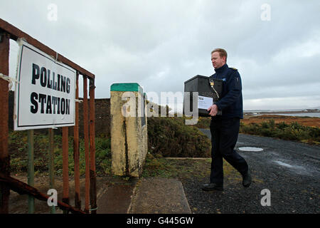 Garda Martin Reilly di Achill arriva con la scatola balot alla stazione di scrutinio di Scoil Mhuire su Inishbiggle (Inis Bigil in irlandese), una piccola isola abitata al largo della costa della contea di Mayo in Irlanda, come il voto ha inizio nelle elezioni generali irlandesi 2011. Il suo nome in irlandese significa "Isola di digiuno" e ha solo 24 elettori iscritti. Foto Stock