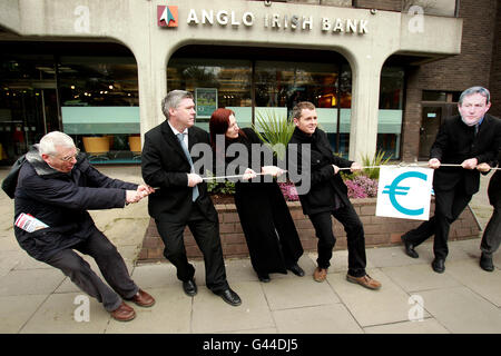 I candidati della United Left Alliance (da sinistra a destra) Joe Higgins, Brian Greene, Claire Daly e Richard Boyd Barrett in un rimorchiatore di guerra con i sostenitori della United Left che indossano le maschere Enda Kenny, Michael Martin ed Eamon Gilmore, durante una campagna stunt fuori dagli uffici della Anglo Irish Bank a Dublino. Foto Stock