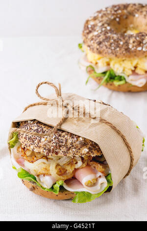 Grano intero tappezzato bagel con cipolla fritti, uova strapazzate, insalata verde e prosciutto crudo su lino bianco tovaglia. Foto Stock