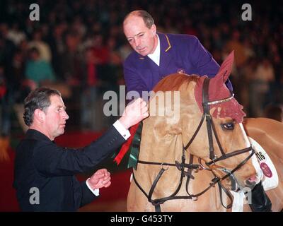 Il Principe del Galles inda una rosetta a 'Virtual Village Grannusch' mentre il pilota John Whitaker guarda a seguire la sua vittoria nel Christmas Turkey Stakes all'Olympia International Showjumping Championships di Londra. *02/12/2000 Whitaker, che si trovava in una condizione critica in ospedale in Svezia dopo aver subito un ictus. Il pilota si trovava a Stoccolma per l'International Horse Show quando si ammalò e si precipitò in ospedale. I funzionari dell'ospedale hanno detto che la sua condizione era stabile dopo che era stato tolto da un ventilatore. Foto Stock