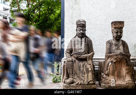 Si affrettò a passanti su un angolo di strada a Hong Kong dove 2 generic statue di divinità cinese di guardia. Foto Stock