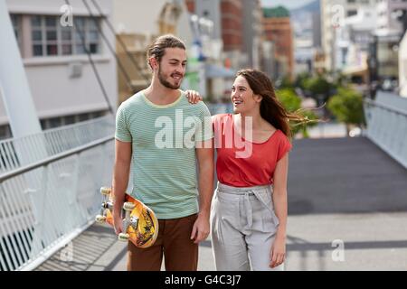 Modello rilasciato. Coppia giovane a piedi, uomo che porta lo skateboard. Foto Stock