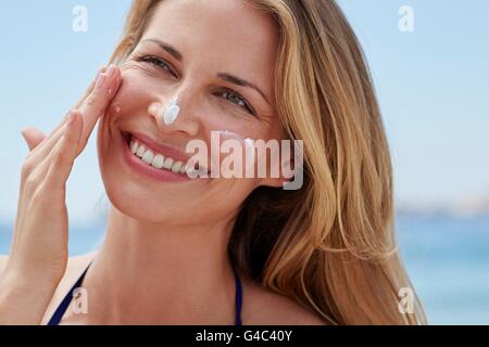 Modello rilasciato. Giovane donna l'applicazione di crema solare per il viso. Foto Stock