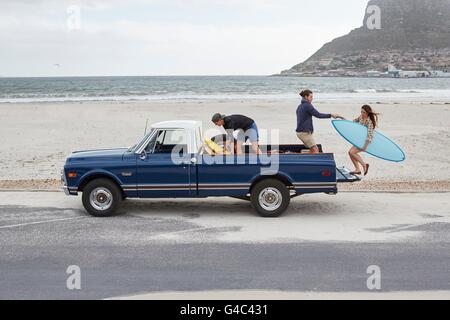 Modello rilasciato. Giovane donna con la tavola da surf essendo aiutato fino in pick up truck sulla spiaggia. Foto Stock