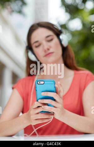 Modello rilasciato. Giovane donna che indossa le cuffie per ascoltare musica sullo smartphone. Foto Stock