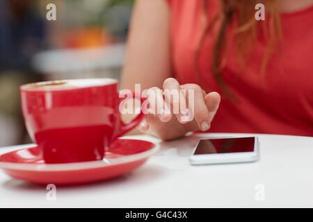 Modello rilasciato. Giovane donna utilizza lo smartphone con caffè, vicino. Foto Stock