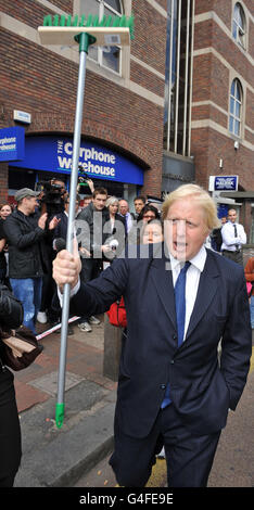 Il sindaco di Londra Boris Johnson detiene un aloft di scopa mentre si rivolge ai membri della comunità fuori dalla stazione ferroviaria di Clapham Junction a seguito di una notte di disordini in tutta Londra e in alcune parti del Regno Unito. Foto Stock