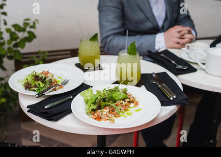 Due piastre di insalata fresca con Rucola, Mozzarella, ortaggi, pomodori, pollo serviti limonata alla menta in un piccolo ristorante all'aperto a pranzo business man sullo sfondo seduti e in attesa per il suo pasto Foto Stock